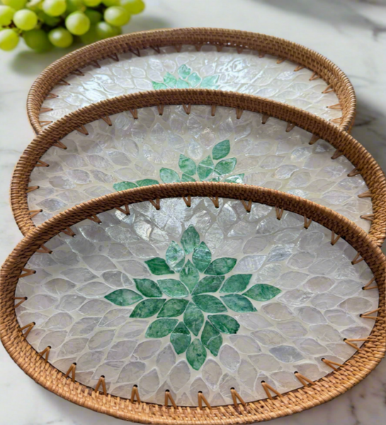 Set of three round woven rattan trays with green leaf patterns on a light surface.