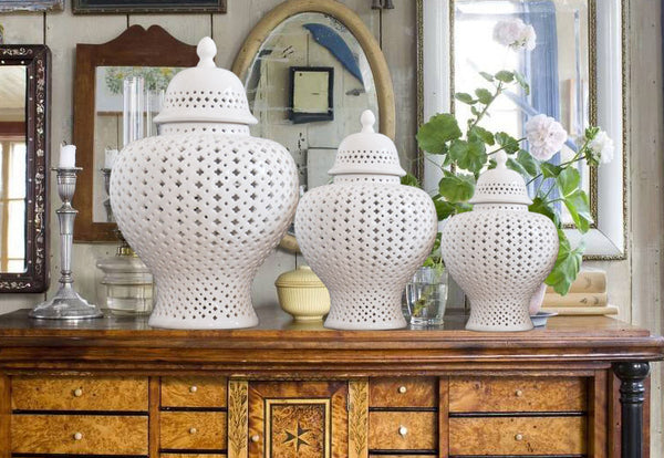 Three white ceramic lattice ginger jars on a vintage wooden sideboard with mirror and greenery